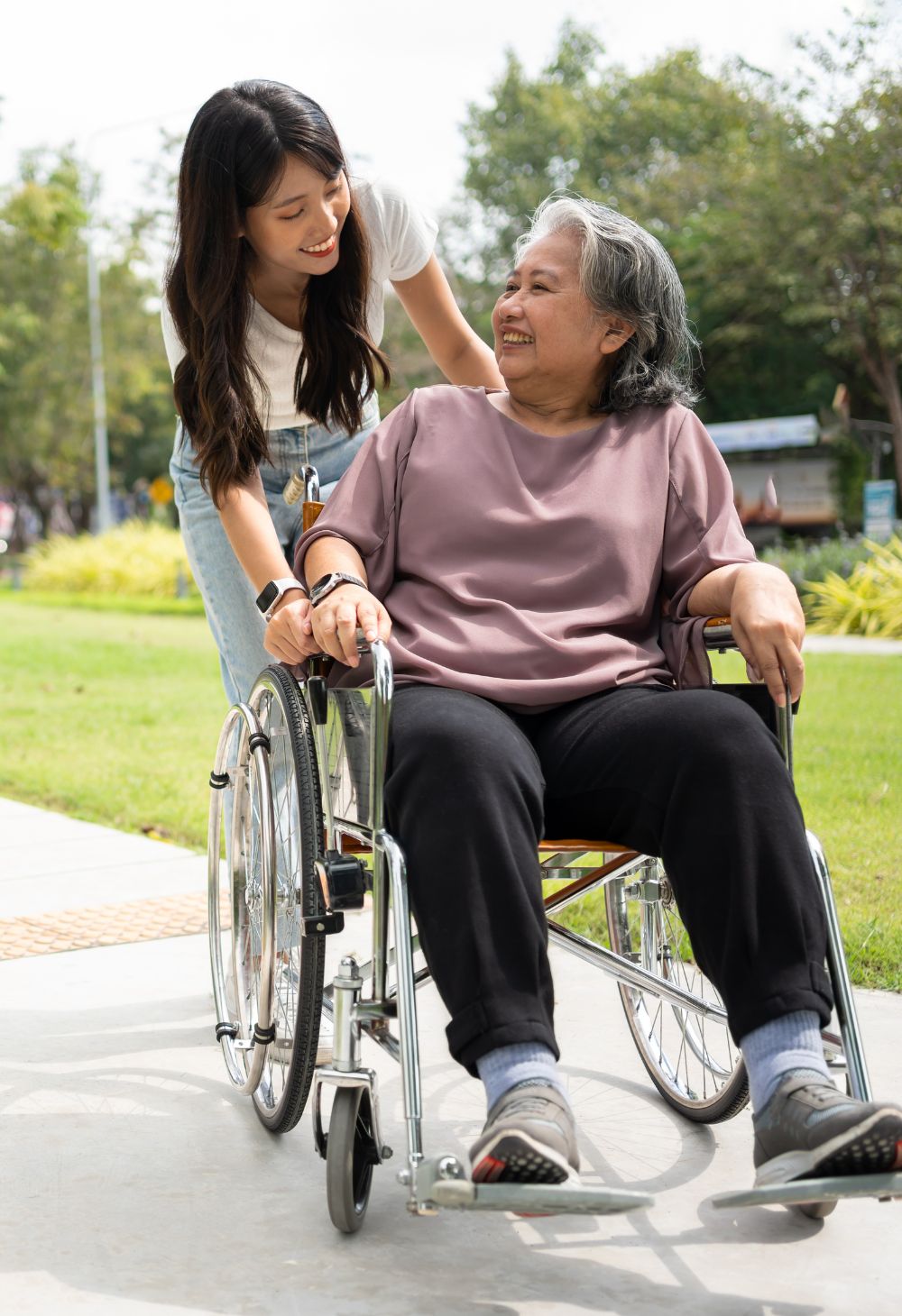 A cheerful care giver pushes an elderly woman in a wheel chair.