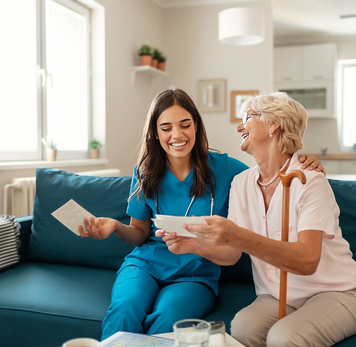 A care giver and elderly patient laugh while sitting on a couch looking at old photos.