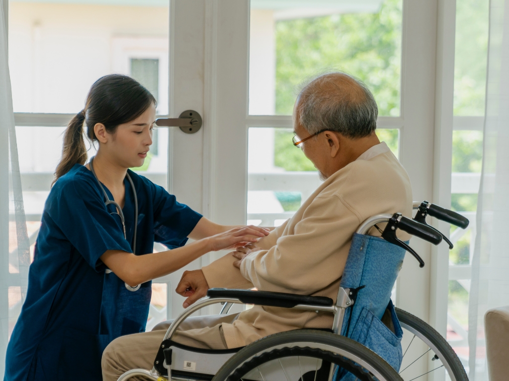 Home Care in Tarrytown Caregiver providing home care in Tarrytown, New York, assisting a senior man in a wheelchair with compassionate support in a bright, comfortable home setting.